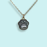 The Shell Paw Print Necklace by Ornamental Things, featuring a paw print-shaped pendant, is displayed against a light blue background.