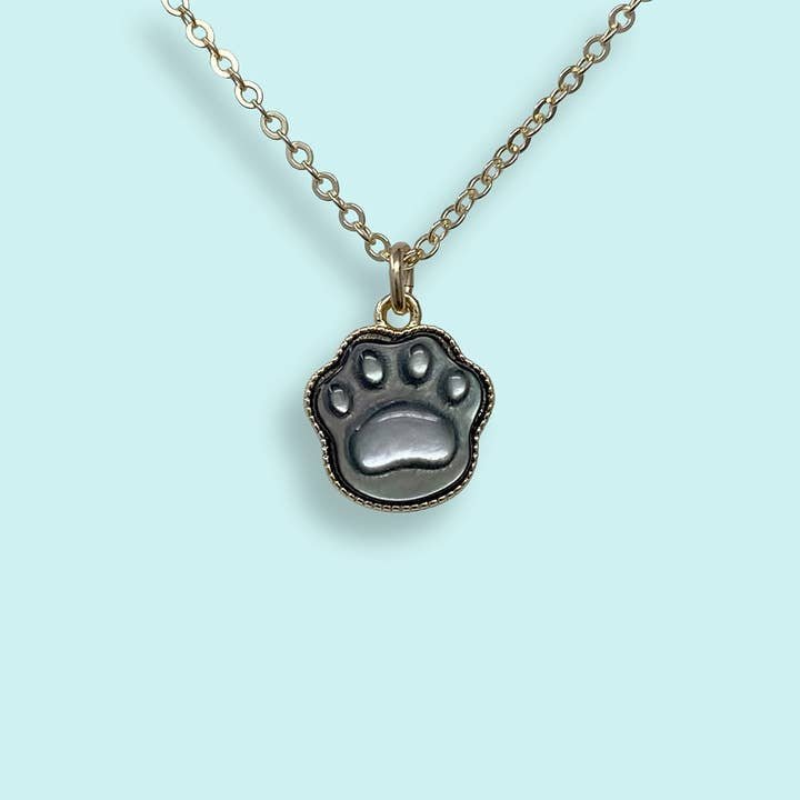 The Shell Paw Print Necklace by Ornamental Things, featuring a paw print-shaped pendant, is displayed against a light blue background.