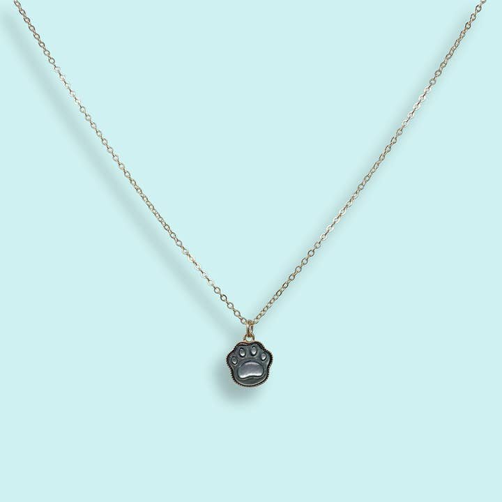 Shell Paw Print Necklace by Ornamental Things—gold-filled chain with a petite black paw print pendant, elegantly shown on a light blue background.