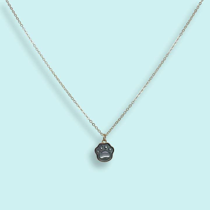The Shell Paw Print Necklace by Ornamental Things features a delicate chain and a small paw print pendant, beautifully showcased on a light blue background.