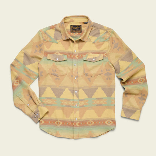 The Howler Brothers Sheridan Flannel Old Gold is a long-sleeve western shirt in a yellow, green, and orange geometric southwestern pattern, made from soft cotton jacquard flannel with two chest pockets and white buttons.