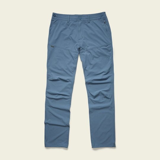 The Shoalwater Tech Pants by Howler Brothers are light blue, straight-leg pants with a front button and zipper, 4-way stretch fabric, two side pockets, and a subtle logo tag on the left hip, shown on a plain background.