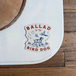 The Ballad of the Bird Dog Shop Cooler Sticker | Pheasant Flush features a pointing dog, birds, plants, and clouds in blue and red. Durable for outdoor use, it stands out on any surface—perfect for coolers or adventures.