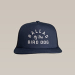 The Ballad of the Bird Dog Shop Hat is a navy blue snapback with an arch logo and white embroidered "Ballad of the Bird Dog" text on the front.