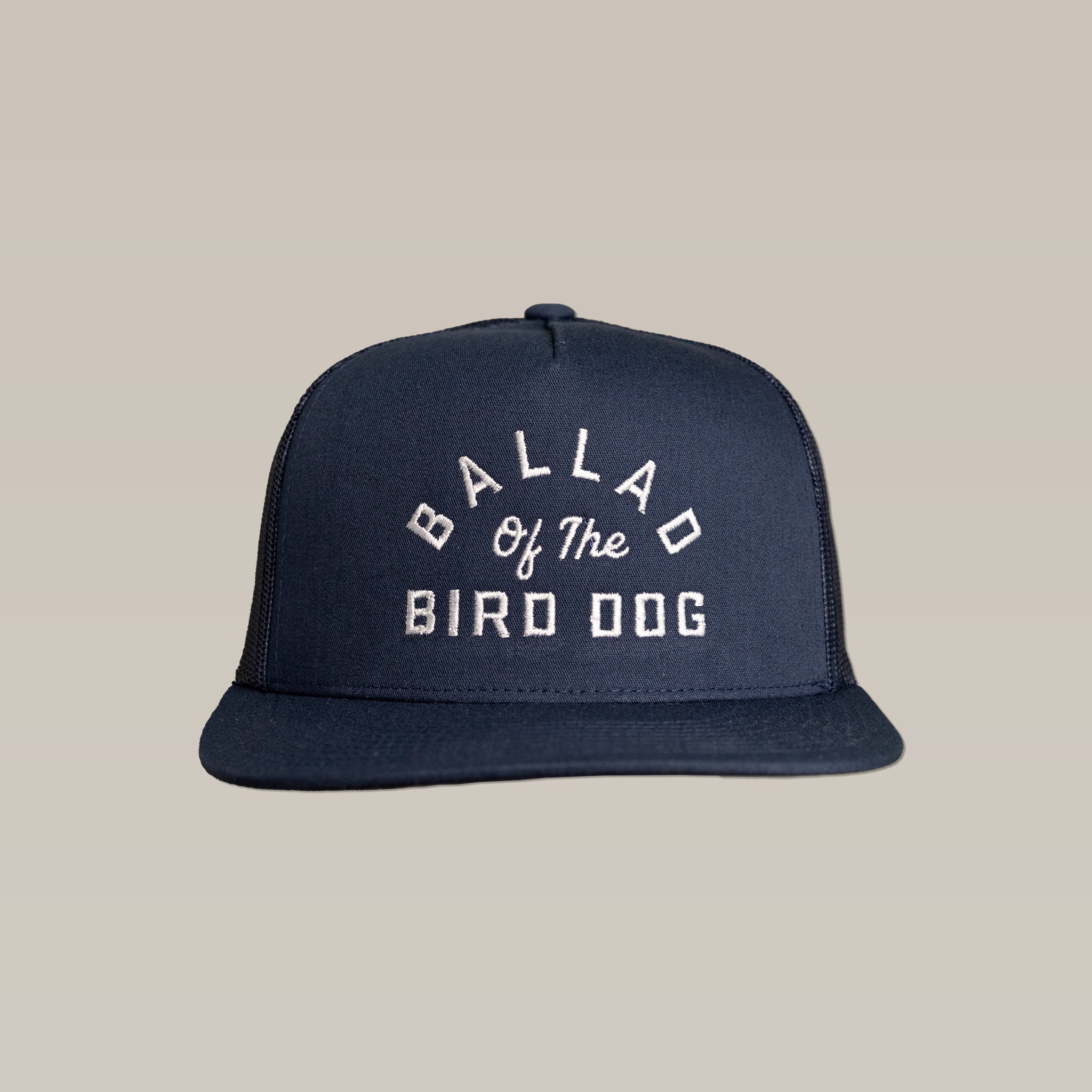 The Ballad of the Bird Dog Shop Hat features a navy blue baseball cap with an arch logo and white embroidered "Ballad of the Bird Dog" text, shown against a plain beige background.