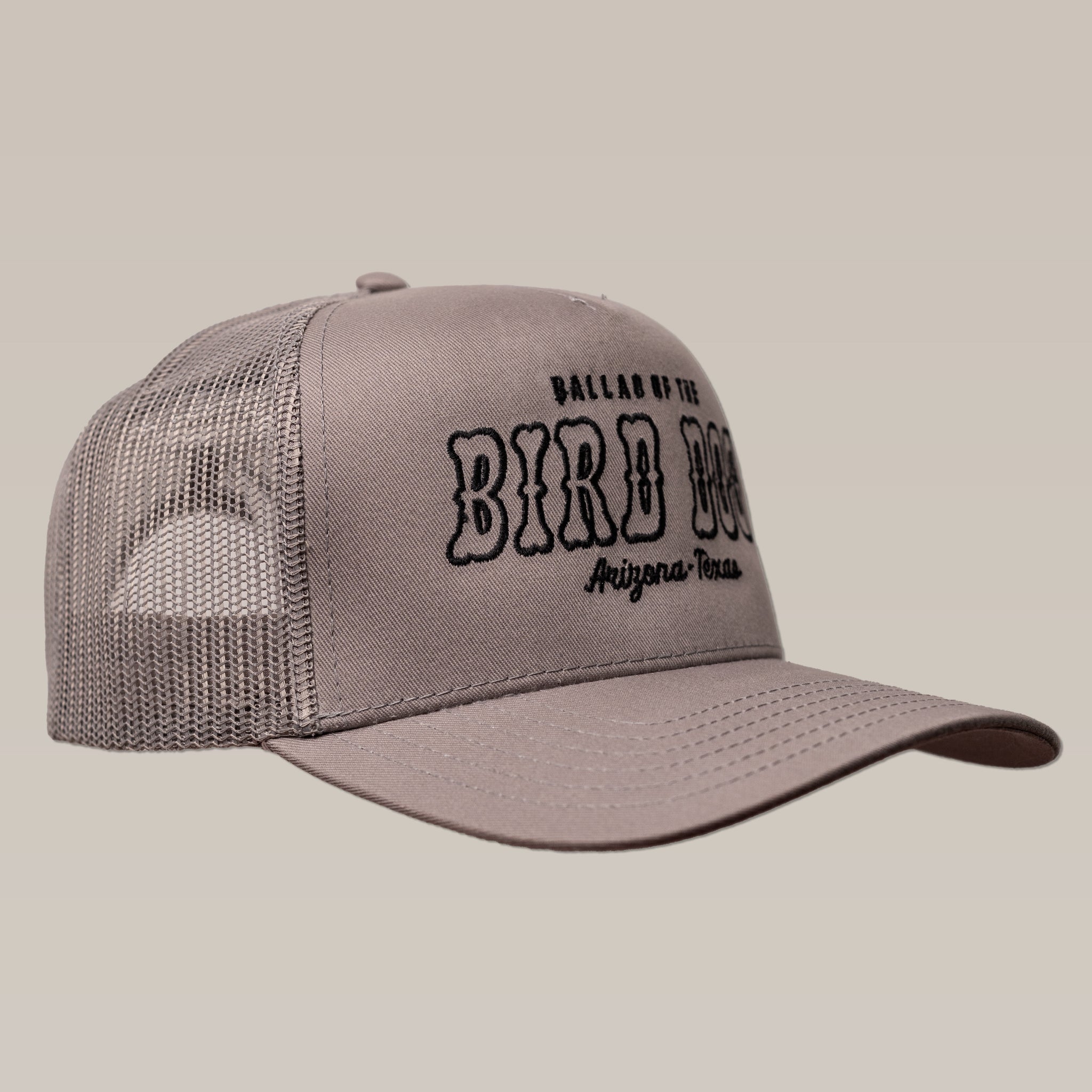 The "Shop Hat | Arizona to Texas" by Ballad of the Bird Dog is a gray mesh trucker hat with "Ballad of the Bird Dog, Arizona, Texas" embroidered in black on the front.