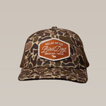 The Ballad of the Bird Dog Shop Hat | Badge features a camouflage design with an orange "Ballad of the Bird Dog, Brenham, Texas" patch, shown against a plain backdrop.