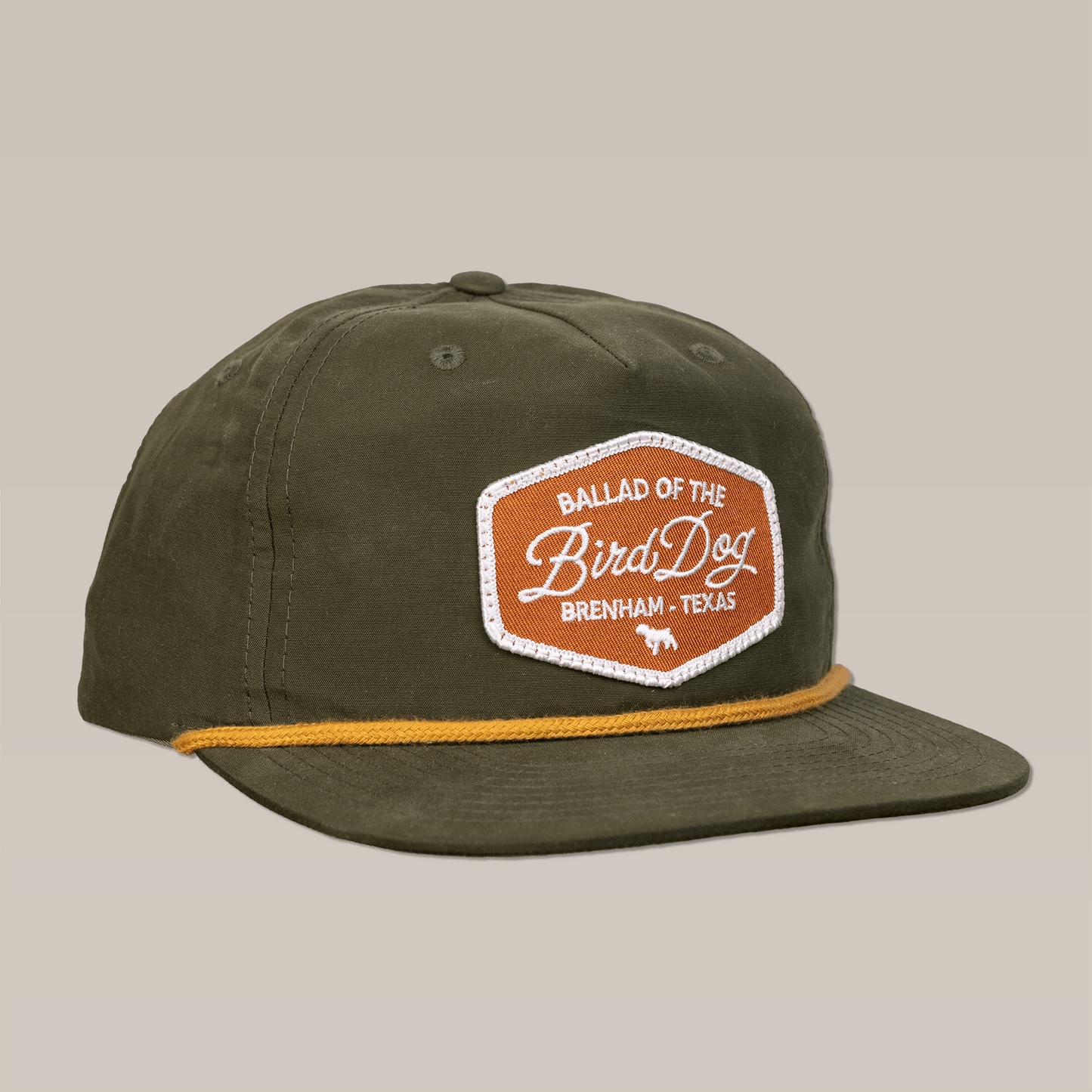 The Shop Hat | Bird Dog Badge by Ballad of the Bird Dog features an olive green design with a yellow cord and brown patch, honoring timeless style and hunting roots.