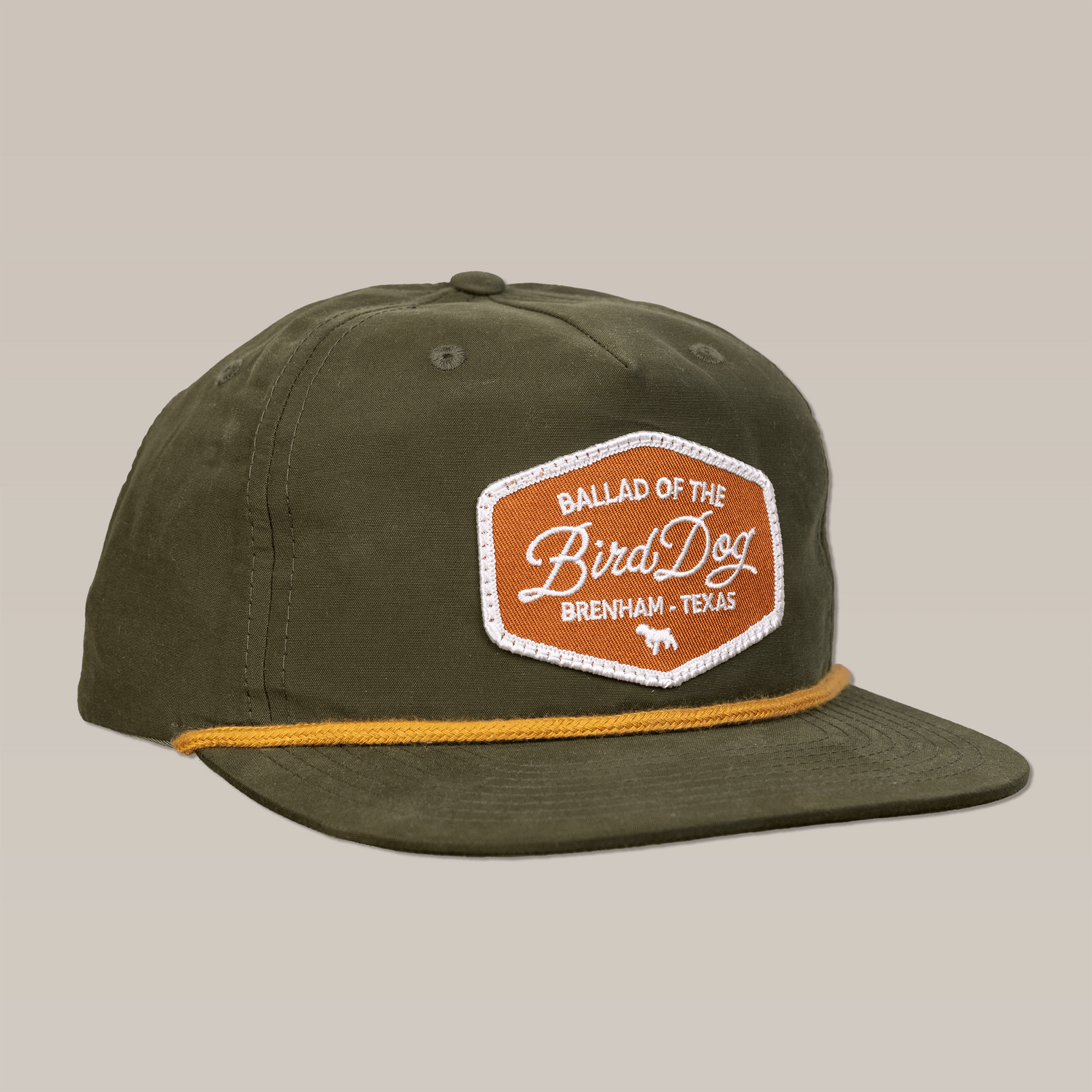The Shop Hat | Bird Dog Badge by Ballad of the Bird Dog features an olive green design with a yellow cord and brown patch, honoring timeless style and hunting roots.