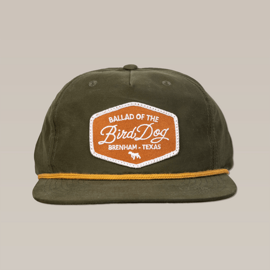 The Ballad of the Bird Dog Shop Hat in olive green features a gold rope detail and a "Ballad of the Bird Dog, Brenham, Texas" patch on front, inspired by vintage hunting badges.