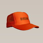 The Shop Hat by Ballad of the Bird Dog features a bright orange mesh back and “BIRDCAGE” boldly embroidered on the front, shown against a beige background.