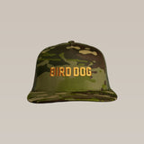 The Shop Hat | Bird Dog Honor by Ballad of the Bird Dog is a camo trucker hat with a mesh back and bold gold "BIRD DOG" embroidery on the front.