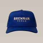 The Shop Hat | Brenham Varsity by Ballad of the Bird Dog features "BRENHAM TEXAS" embroidered in white on a blue cap, celebrating local heritage and displayed against a simple, light background.