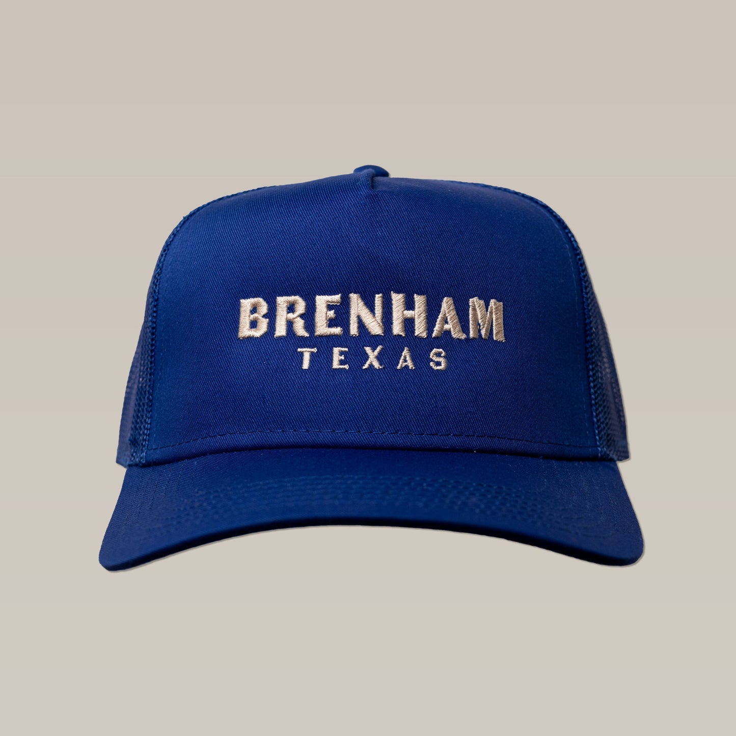 The Shop Hat | Brenham Varsity by Ballad of the Bird Dog is a blue trucker hat featuring "Brenham Texas" embroidered in white on the front, shown against a plain beige background.