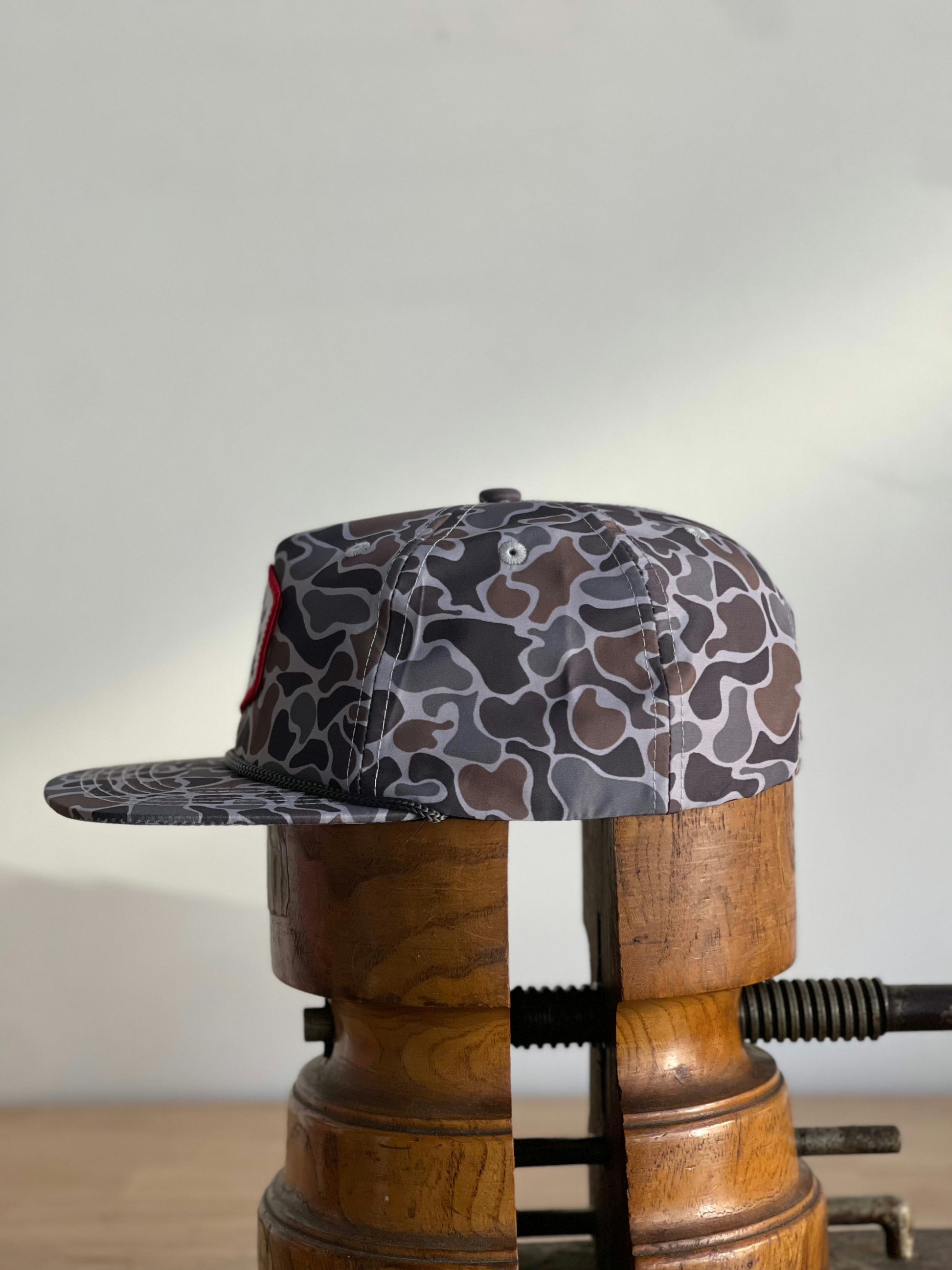 The Ballad of the Bird Dog Shop Hat | Camo Companion is shown on a wooden hat press against a plain background—perfect outdoor headwear for stylish camouflage.