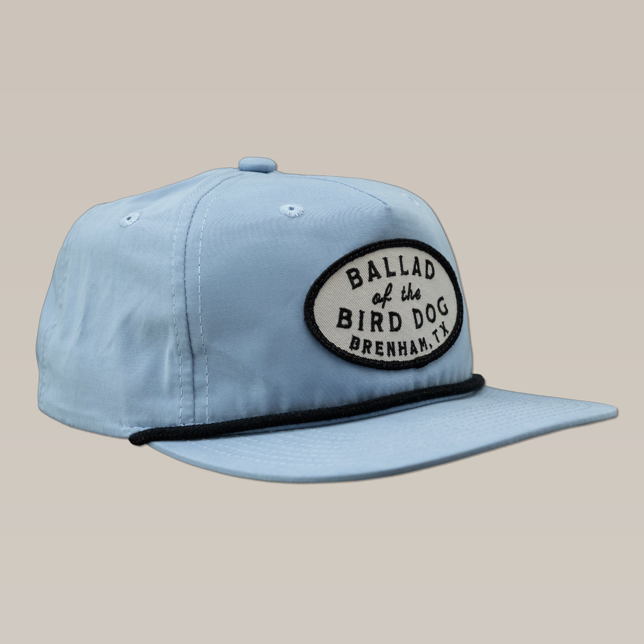 The Ballad of the Bird Dog Shop Hat features a light blue design, a black oval "Ballad of the Bird Dog Brenham, TX" patch on the front, and a black rope detail above the brim.
