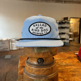 The Shop hat by Ballad of the Bird Dog, featuring the Classic Shop Logo patch, is showcased on a vintage wooden hat block in a rustic shop.