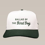 The Ballad of the Bird Dog Desert Series Shop Hat is a white and dark green baseball cap with "BALLAD OF THE Bird Dog" embroidered on the front in green and black.