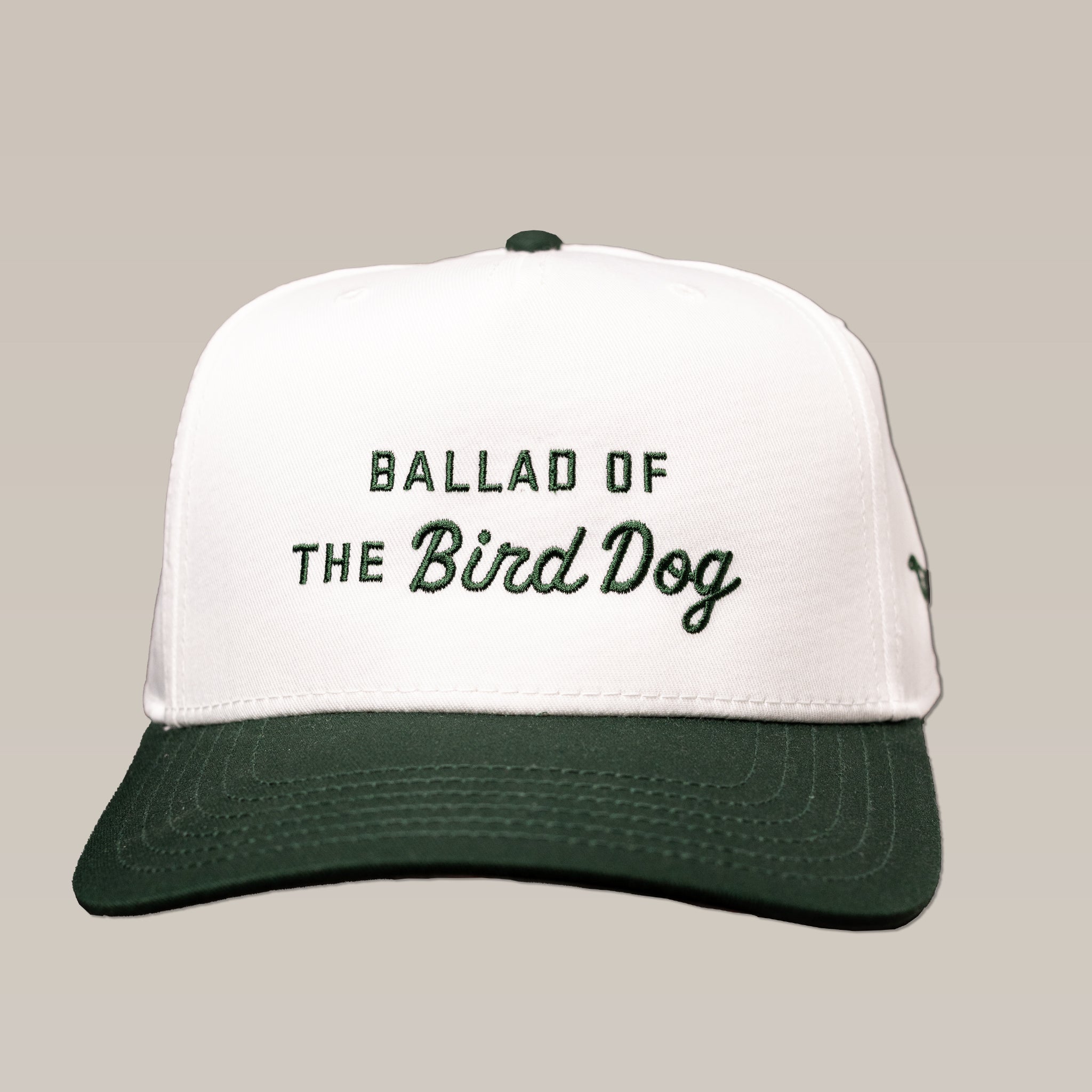 The Ballad of the Bird Dog Desert Series Shop Hat is a white and dark green baseball cap with "BALLAD OF THE Bird Dog" embroidered on the front in green and black.