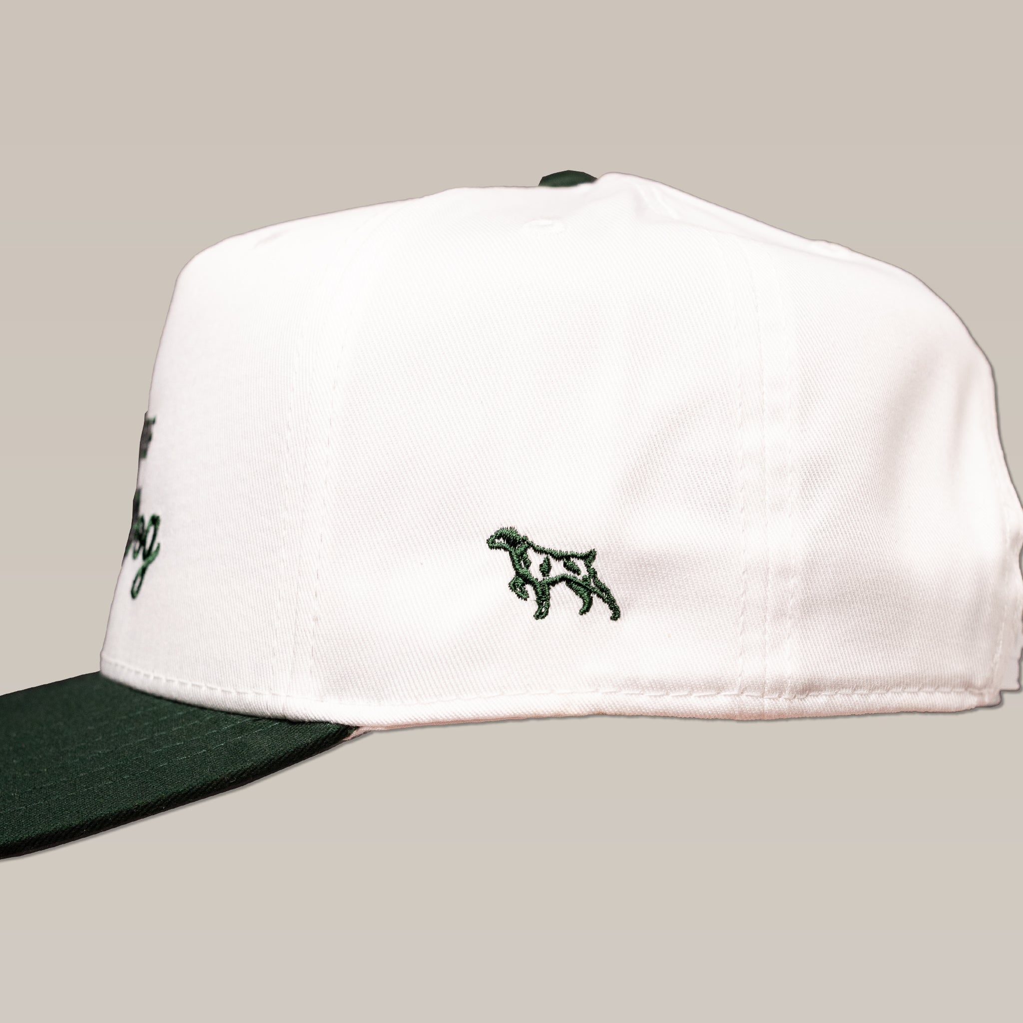 The Ballad of the Bird Dog Shop Hat | Desert Series features a white cap with a dark green brim and a small embroidered dog outline on the side.