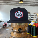The Ballad of the Bird Dog Shop Hat | Field Companion, featuring a red and white “Ballad of the Bird Dog Texas” patch, is displayed on a vintage wooden stand in a workshop amid sewing supplies.