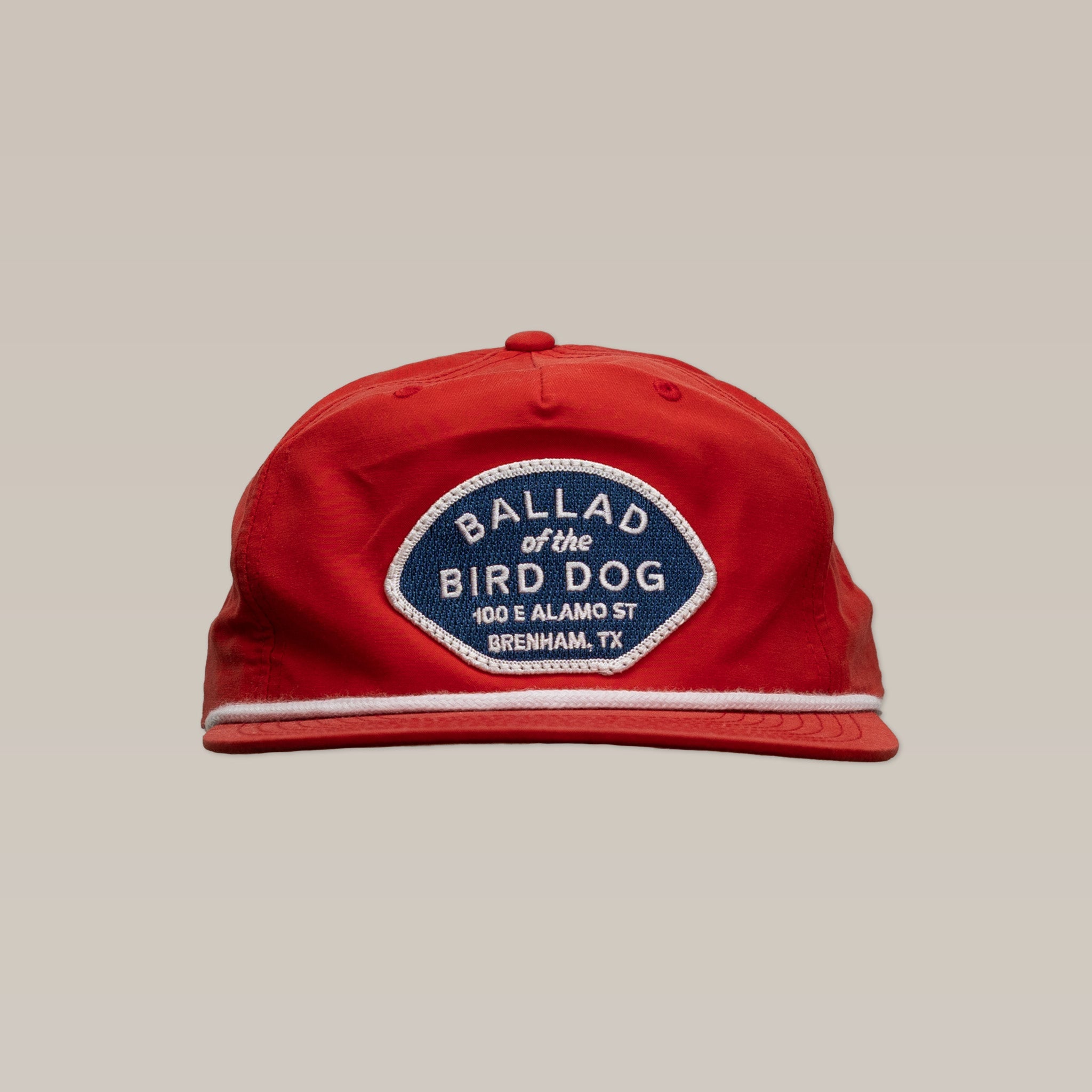 The Shop Hat | Home Base by Ballad of the Bird Dog is a red hat with a blue and white patch reading "BALLAD of the BIRD DOG, 100 E ALAMO ST, BRENHAM, TX"—a standout small business hat for showing community spirit.