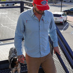 A man in a light blue shirt wearing the Ballad of the Bird Dog Shop Hat | Home Base walks up outdoor metal stairs with his black and white dog. The parking lot and buildings in the background highlight community style.