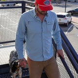 A man in a Ballad of the Bird Dog Shop Hat (Home Base) and a light blue shirt walks up an outdoor metal staircase with a black and white dog beside him.