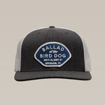 The Shop Hat | Home Base by Ballad of the Bird Dog is a gray and white trucker hat with a blue and white patch reading "Ballad of the Bird Dog, 100 E Alamo St, Brenham, TX," ideal for community headwear fans.