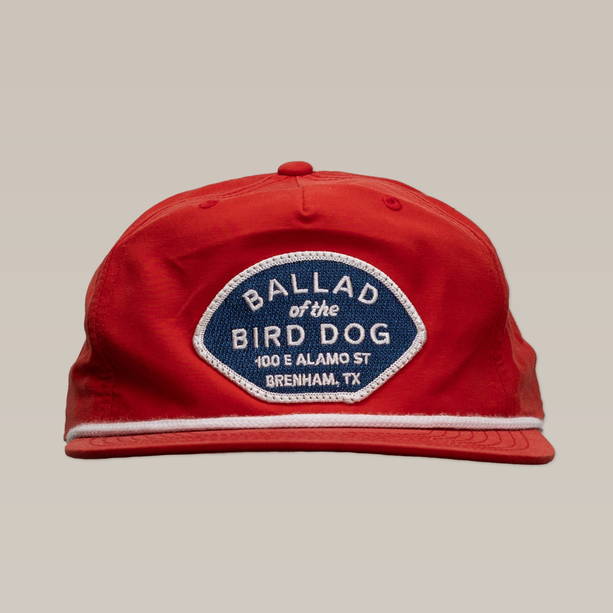 The Shop Hat | Home Base by Ballad of the Bird Dog is a red cap featuring a blue and white patch reading "Ballad of the Bird Dog, 100 E Alamo St, Brenham, TX"—a great way to support a local small business and community.