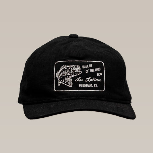 The Ballad of the Bird Dog Shop Hat | La Lobina is a black angler hat with a white embroidered fish patch and "Ballad of the Bird Dog" branding.