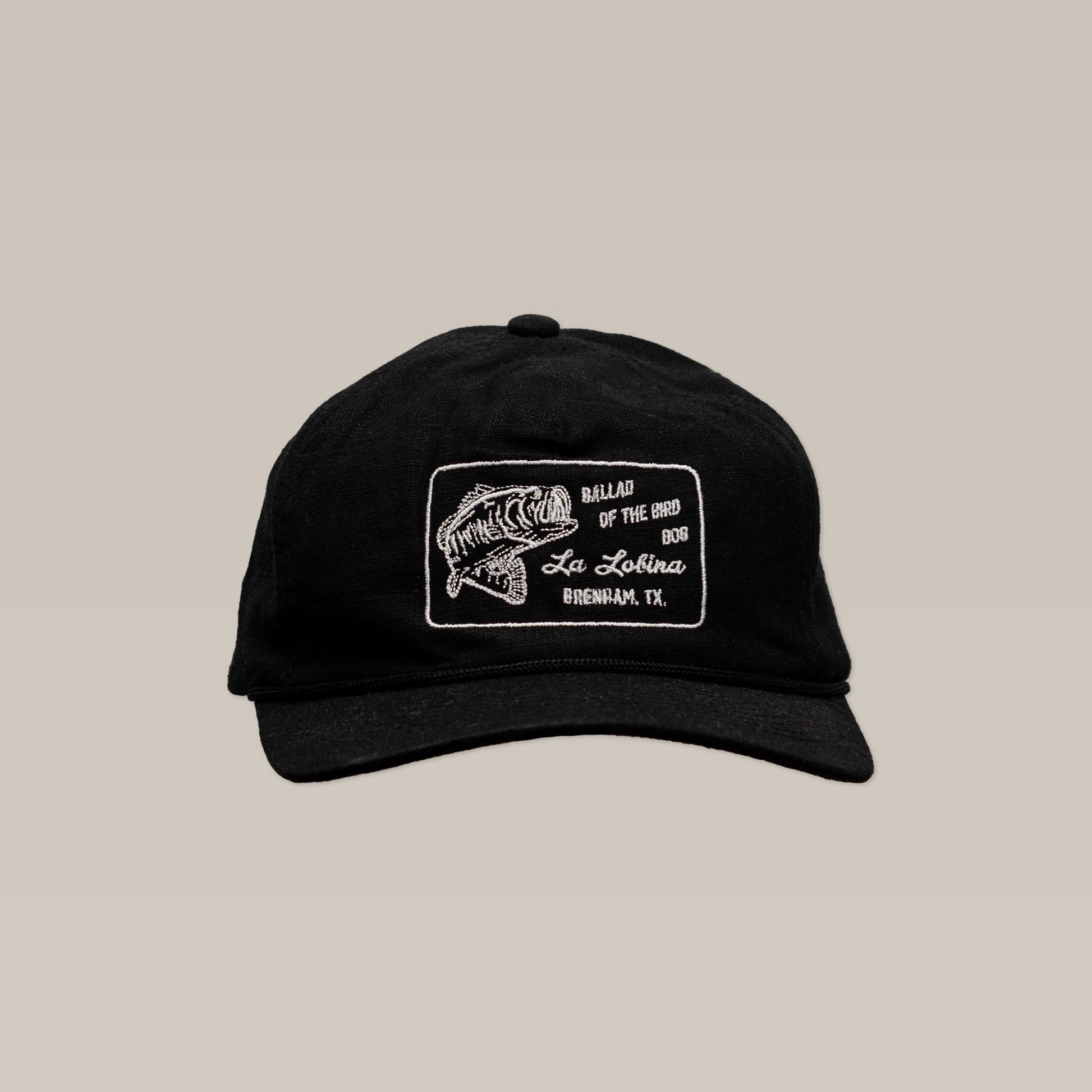 The Shop Hat | La Lobina by Ballad of the Bird Dog is a black angler hat with a white embroidered fish patch and text: "Ballad of the Big Bass, La Lobina Bass Fishing Hat, Brenham, TX.