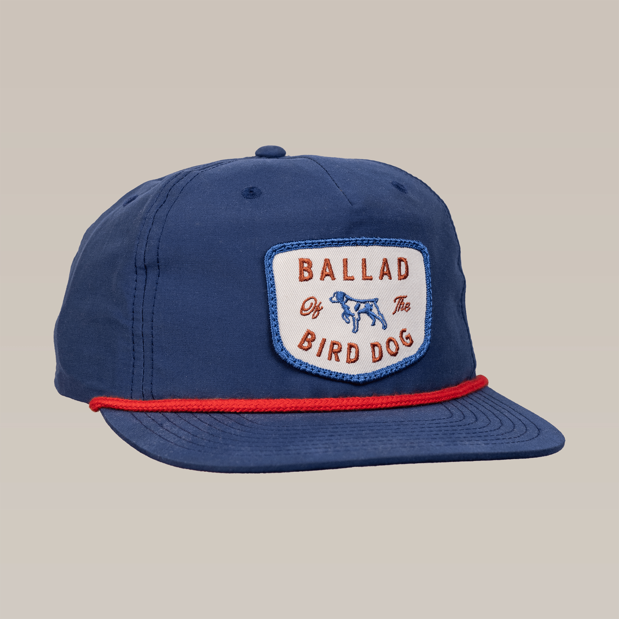 The Shop Hat | Legend by Ballad of the Bird Dog is a blue baseball cap with a red rope brim and front patch featuring "Ballad of the Bird Dog" and a dog illustration, inspired by classic Americana and the Legend of the Bird Dog.