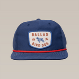 The Shop Hat | Legend by Ballad of the Bird Dog is a blue cap with a white "Ballad of the Bird Dog" patch, blue dog illustration, red cord above the brim, and vintage Americana hunting hat style.