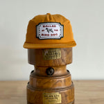 A Shop Hat | Neon Revival by Ballad of the Bird Dog, featuring a branded patch, sits on a wooden piece decorated with engraved brass labels.