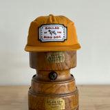 The Shop Hat | Neon Revival by Ballad of the Bird Dog, featuring the classic logo patch, sits on a vintage wooden object with brass labels—reflecting downtown Brenham style.