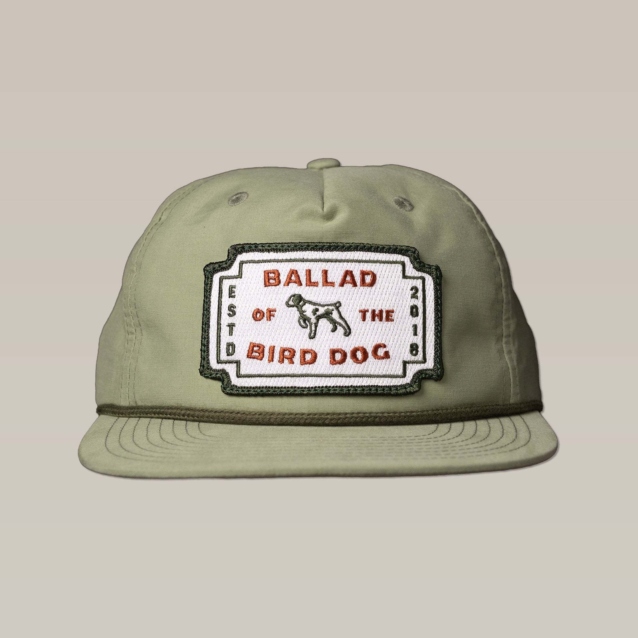 The Shop Hat | Neon Revival by Ballad of the Bird Dog features a light olive green design with a classic logo patch, dog illustration, and "ESTD 2018"—a stylish way to show your love for downtown Brenham.