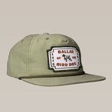 The Shop Hat | Neon Revival by Ballad of the Bird Dog features an olive green classic logo and a rectangular patch with "Ballad of the Bird Dog" and a bird dog graphic, inspired by downtown Brenham.