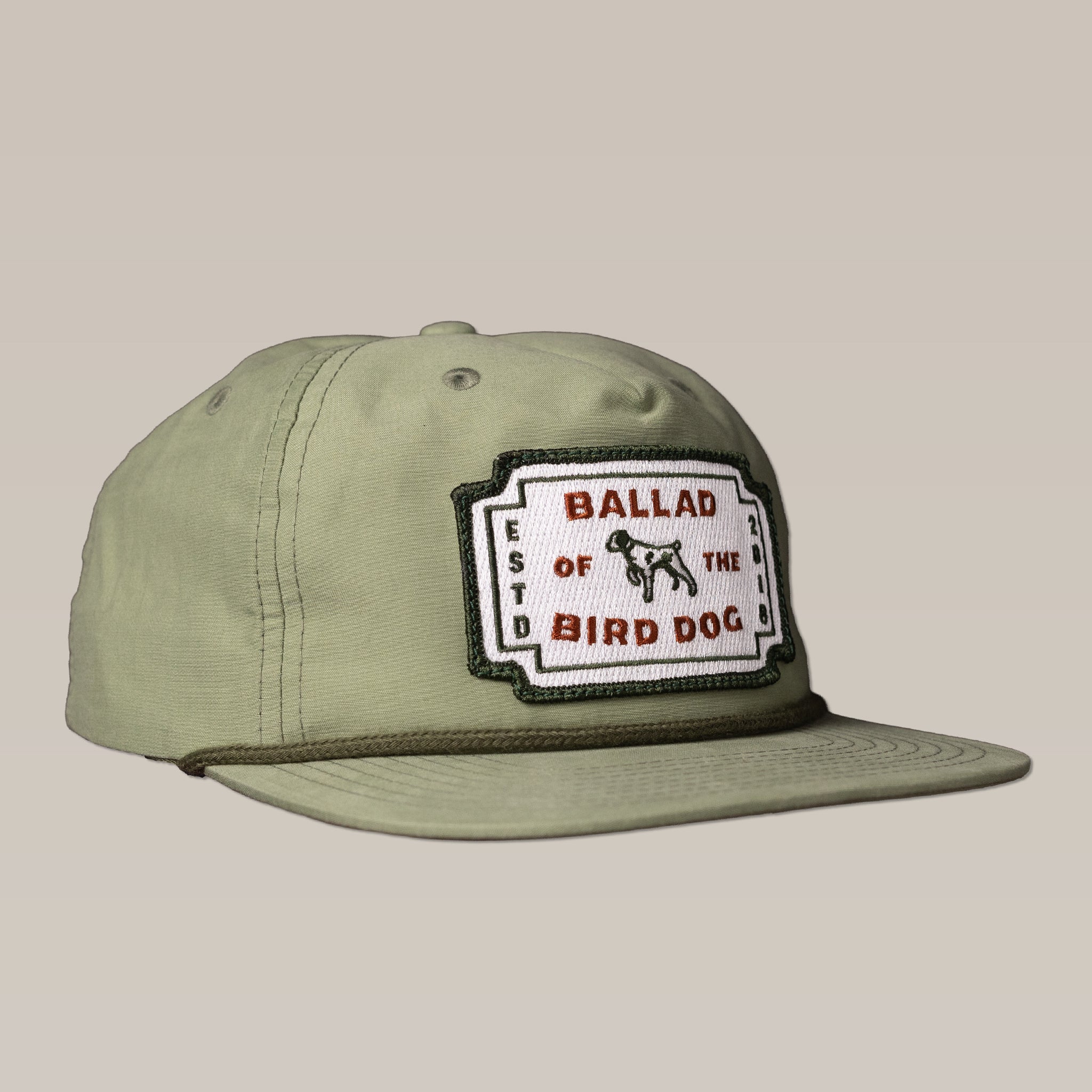 The Shop Hat | Neon Revival by Ballad of the Bird Dog features an olive green classic logo and a rectangular patch with "Ballad of the Bird Dog" and a bird dog graphic, inspired by downtown Brenham.