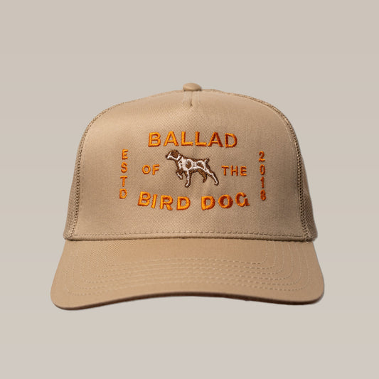The "Shop Hat | Neon Sign" by Ballad of the Bird Dog is a tan trucker hat featuring orange embroidery with the brand name, a dog illustration, and "ESTD 2018" on the front.