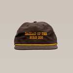 The Shop Hat | Old Fashioned by Ballad of the Bird Dog features brown fabric, yellow "BALLAD OF THE BIRD DOG" embroidery, and a yellow stripe above the brim—a classic western hat for a rustic look.