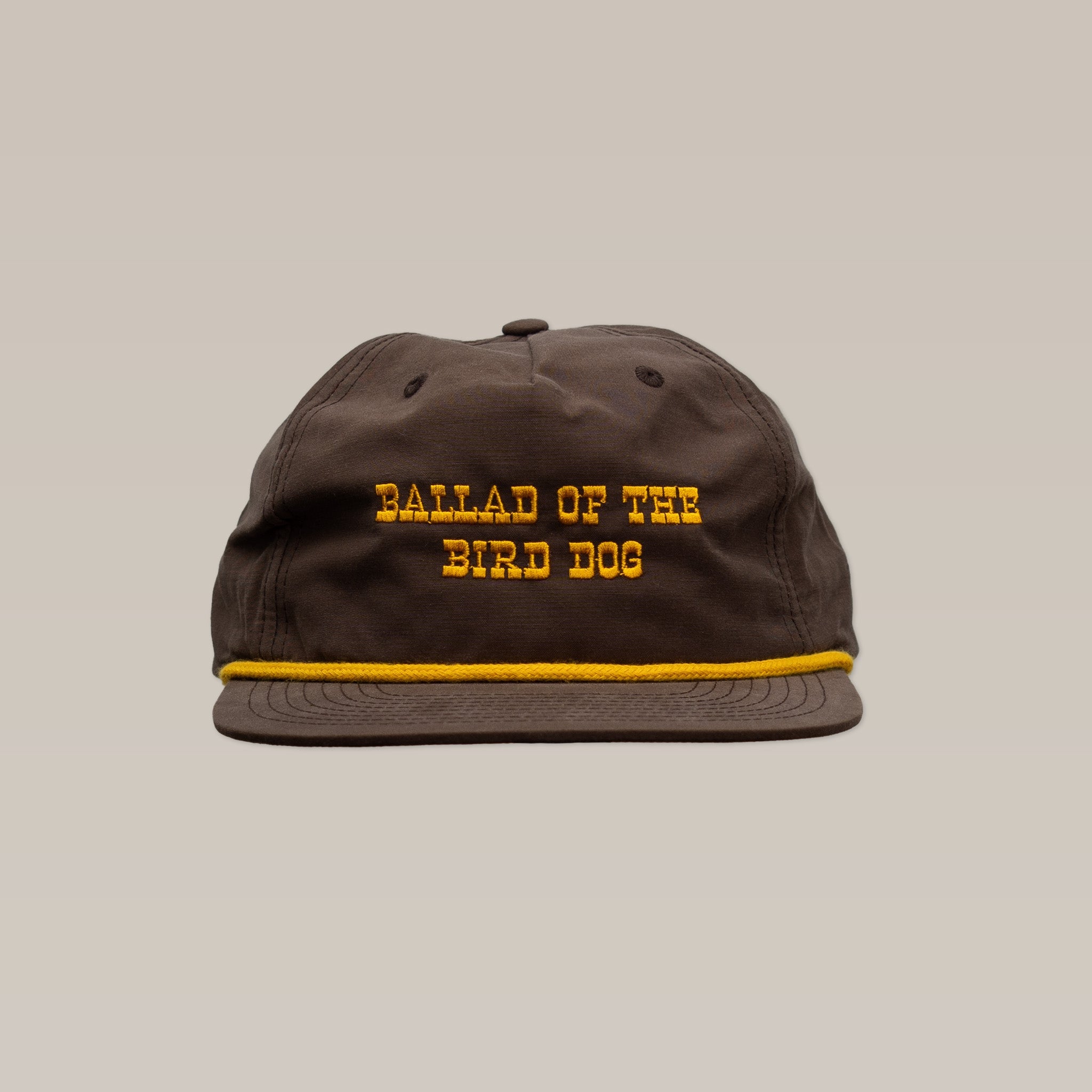 The Shop Hat | Old Fashioned by Ballad of the Bird Dog features brown fabric, “BALLAD OF THE BIRD DOG” yellow embroidery on the front, and a yellow-trimmed brim—offering classic Western charm against a plain background.