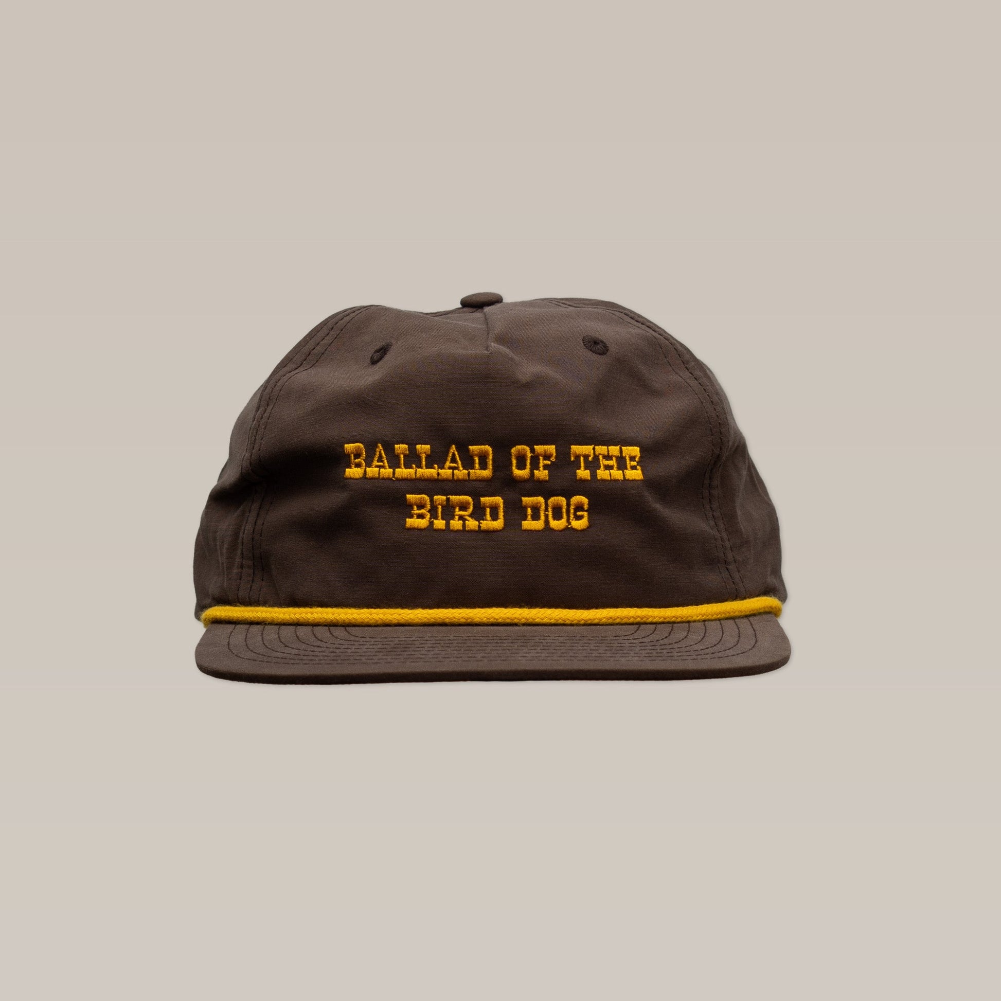 The Shop Hat | Old Fashioned by Ballad of the Bird Dog is a brown cap with yellow "BALLAD OF THE BIRD DOG" embroidery and a yellow stripe above the brim, shown against a plain beige background.