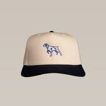 The Shop Hat | Pointer by Ballad of the Bird Dog features a beige and black design with a blue and white embroidered pointing bird dog on the front, perfect for your next outdoor adventure.