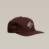 The Shop Hat | Red Tailed Hawk by Ballad of the Bird Dog is a brown baseball cap featuring white embroidered artwork of a hand and skateboard on the front, displayed against a plain beige background.