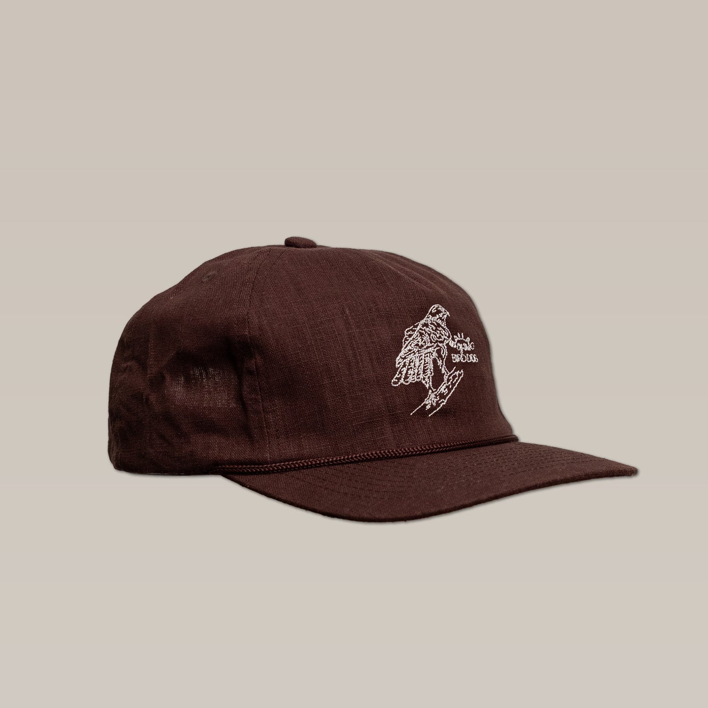 The Shop Hat | Red Tailed Hawk by Ballad of the Bird Dog is a brown baseball cap featuring a white embroidered hand design and text on the front, shown against a plain beige background.
