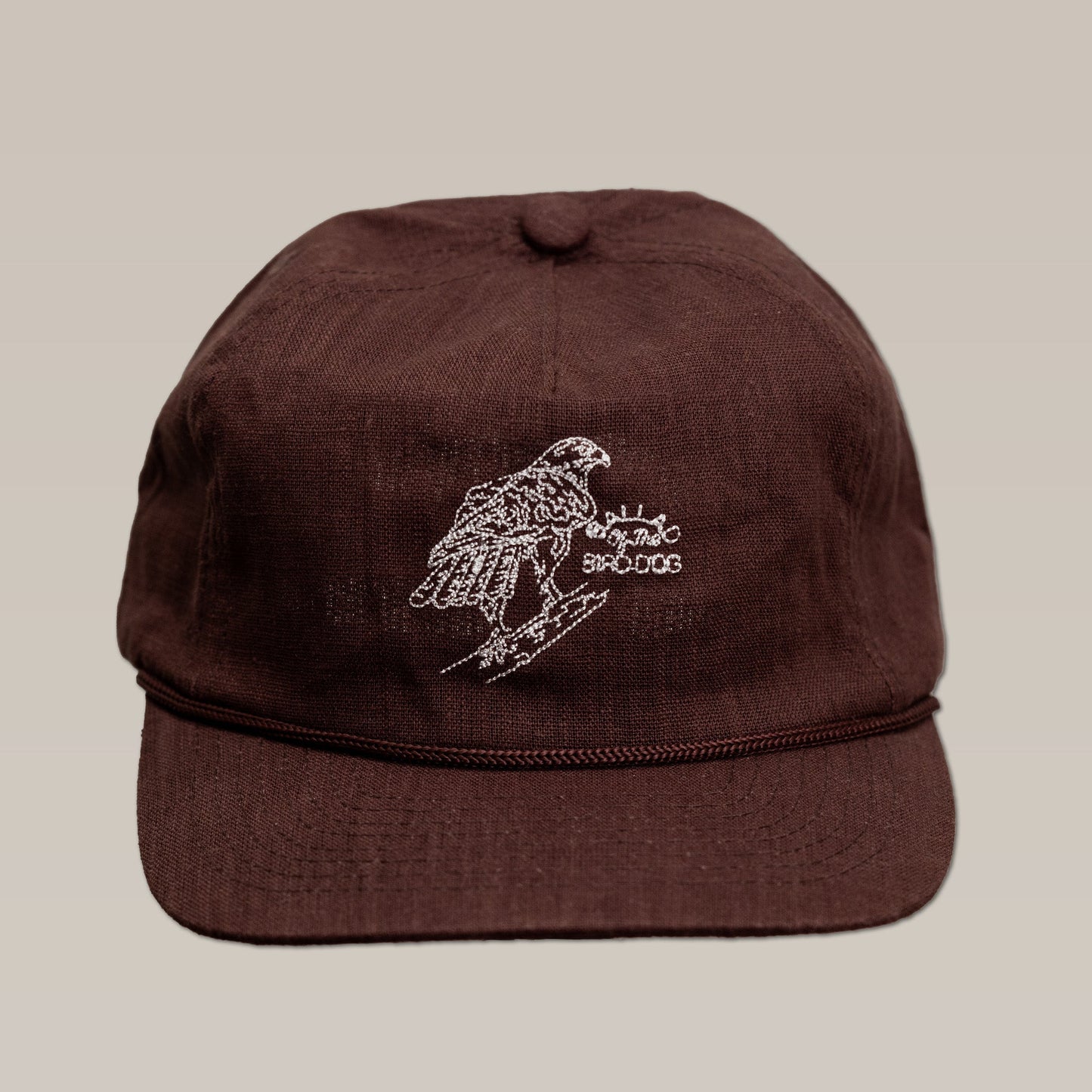 Brown Shop Hat by Ballad of the Bird Dog, featuring a white embroidered red-tailed hawk perched on a branch and stylized text, displayed against a plain background.