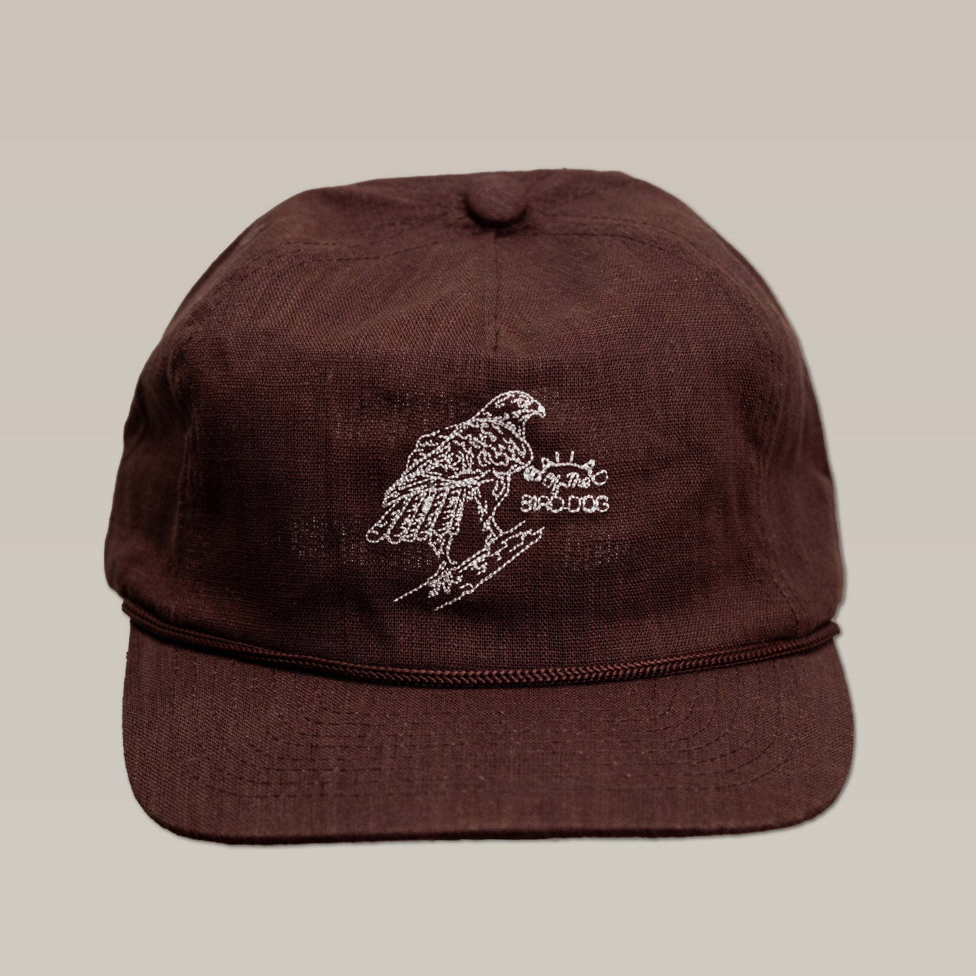 Brown Shop Hat by Ballad of the Bird Dog, featuring a white embroidered red-tailed hawk perched on a branch and stylized text, displayed against a plain background.