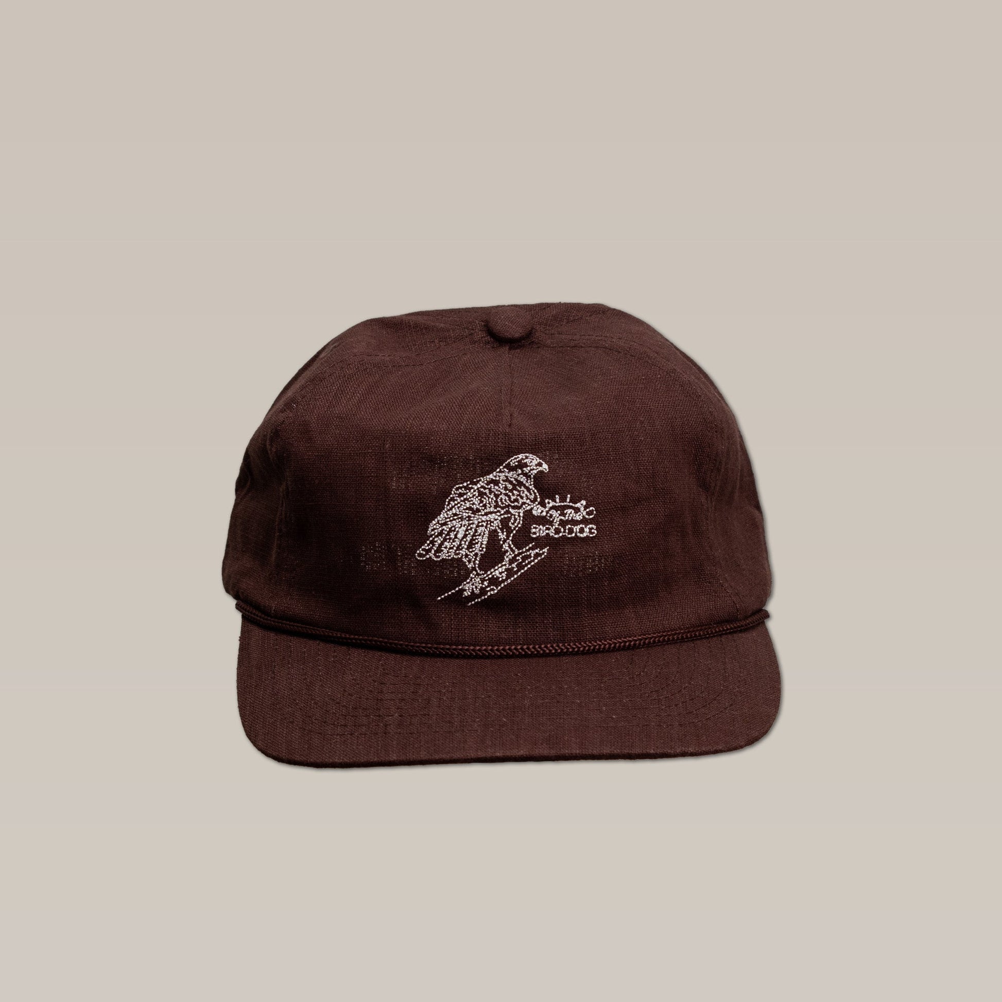 The Shop Hat by Ballad of the Bird Dog is a brown baseball cap featuring an embroidered red-tailed hawk perched on a branch, shown against a plain beige background.