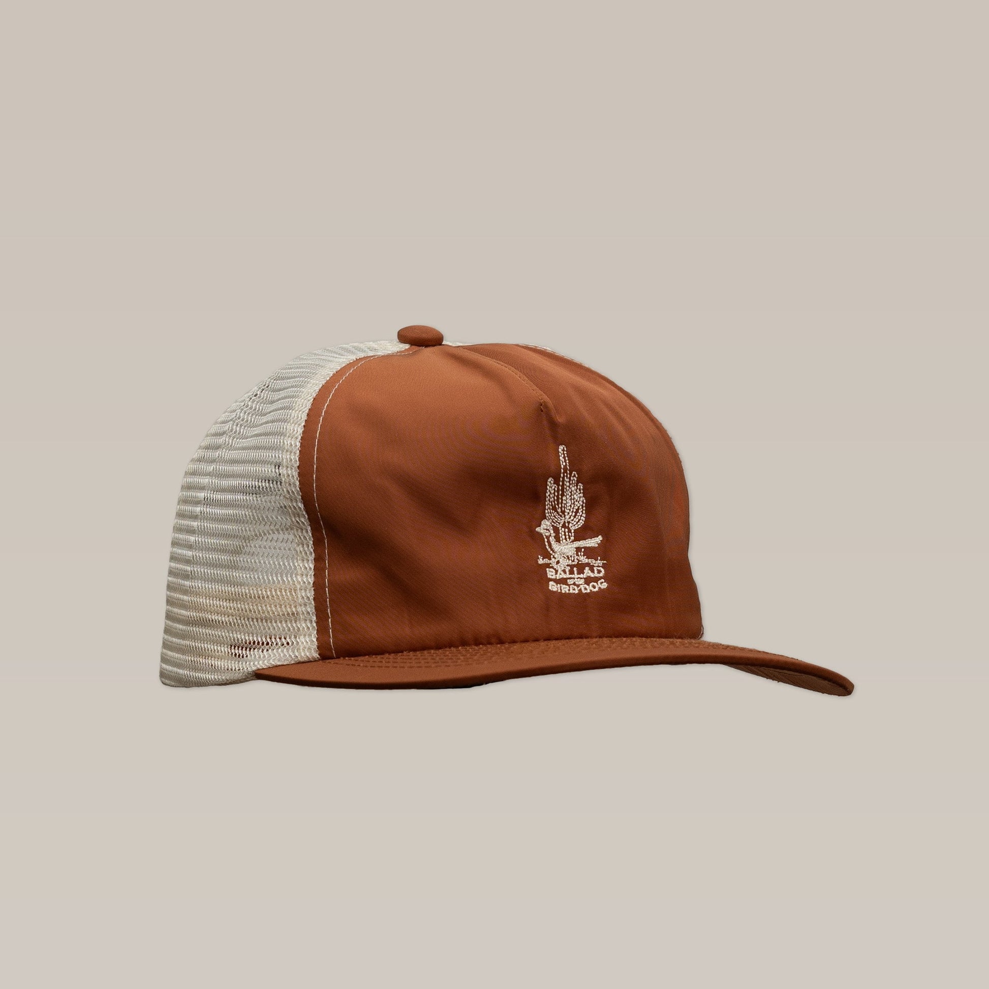 The Shop Hat | Roadrunner Saguaro by Ballad of The Bird Dog is a brown and white mesh trucker hat featuring an embroidered desert motif, shown against a neutral background.